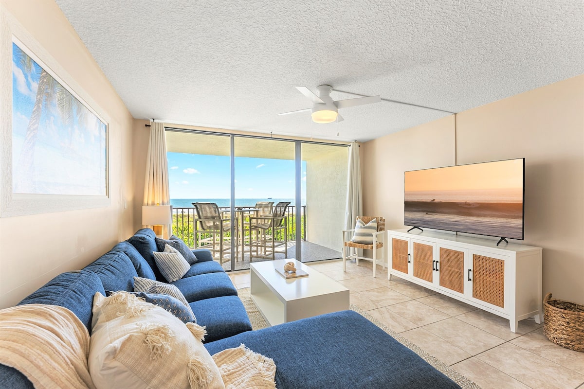 Een moderne woonkamer met een bank, televisie en een balkon met uitzicht op de oceaan.