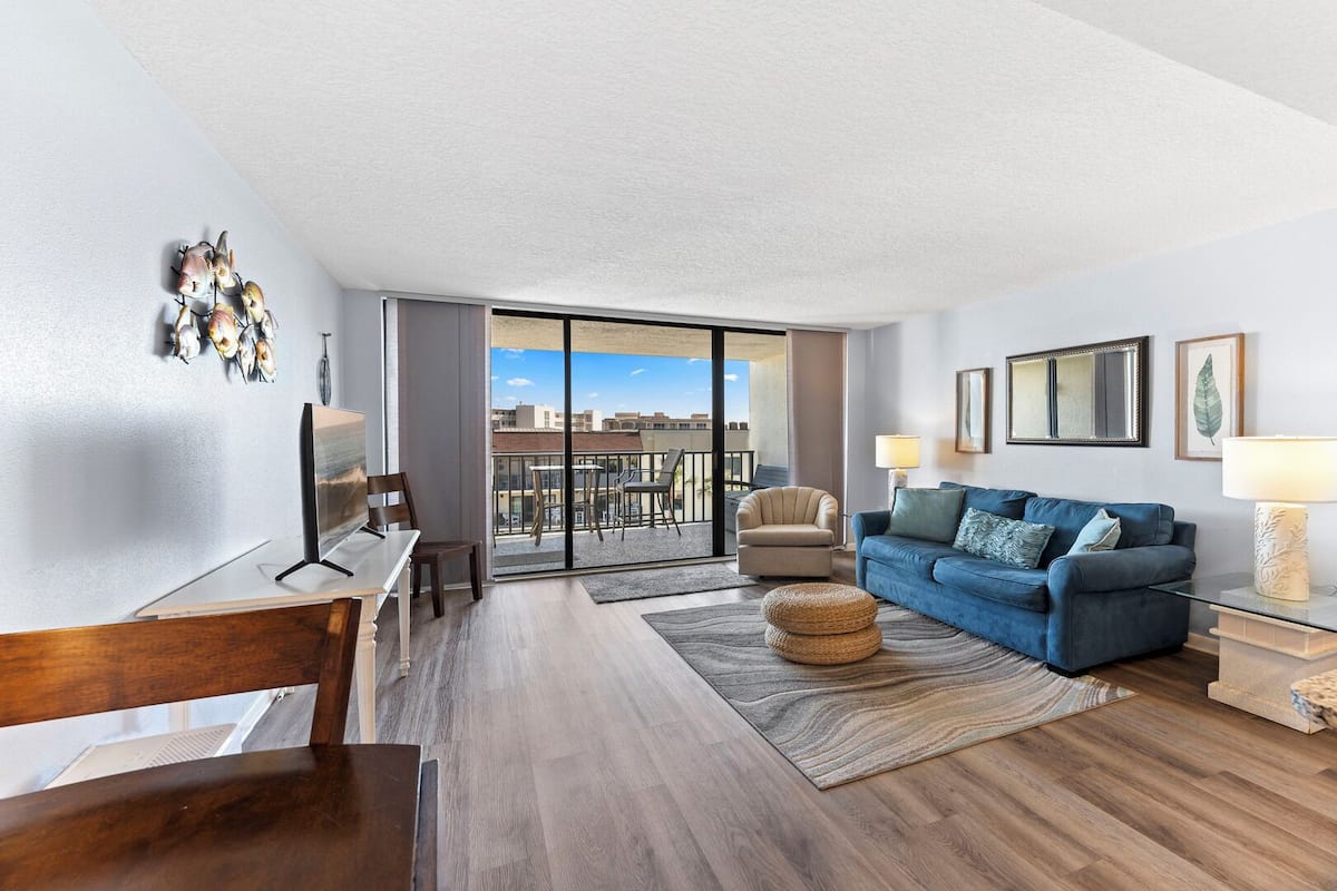 Een moderne woonkamer met een blauwe bank, een eettafel en een balkon met uitzicht op de stad.