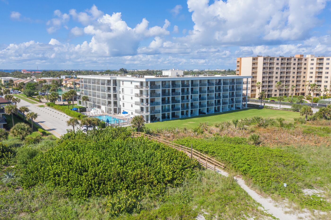 Een modern hotel met een zwembad, omringd door groen en een heldere lucht.
