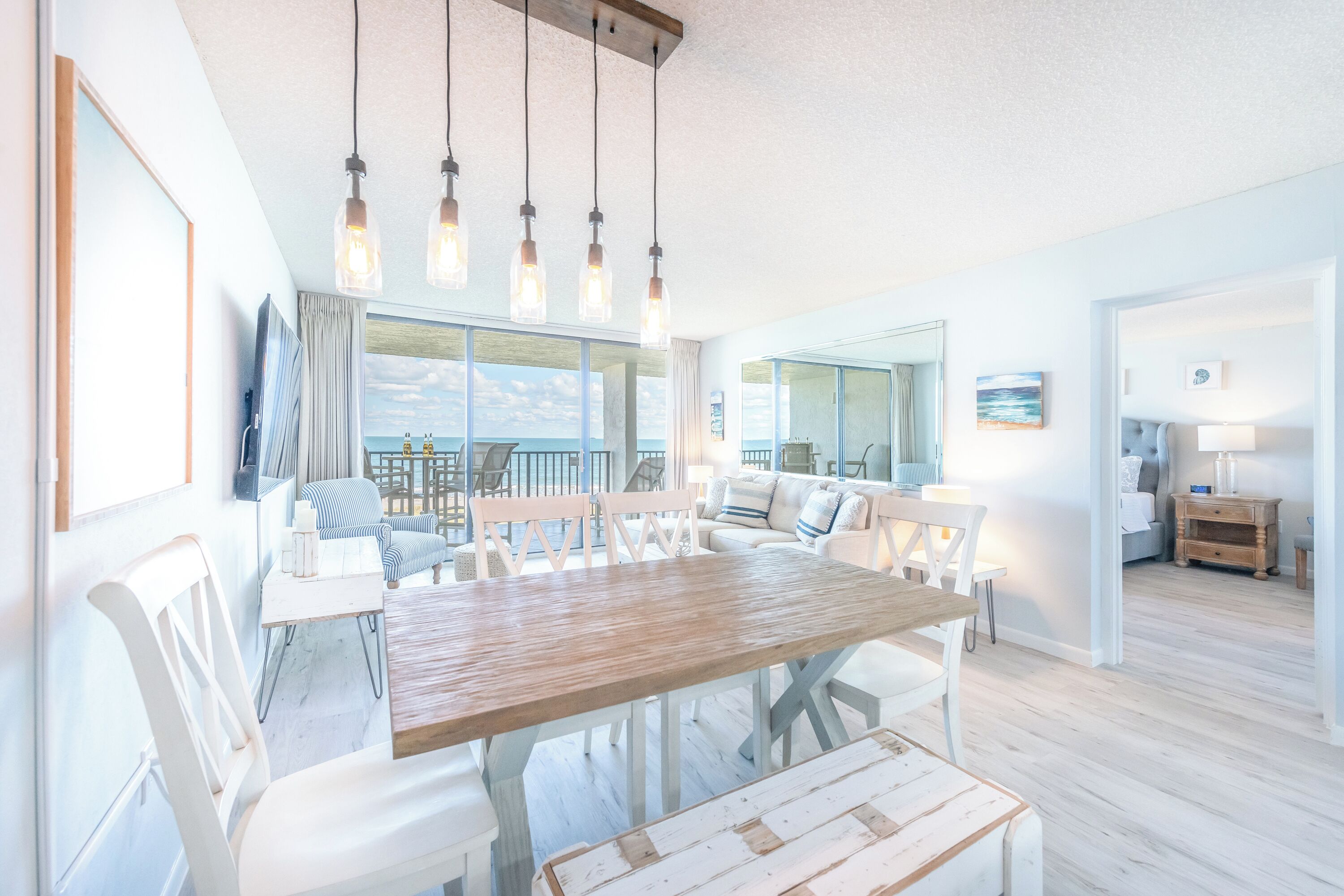 Un'ampia sala da pranzo con un tavolo in legno e sedie bianche, un'ampia finestra con vista e una cucina moderna sullo sfondo.