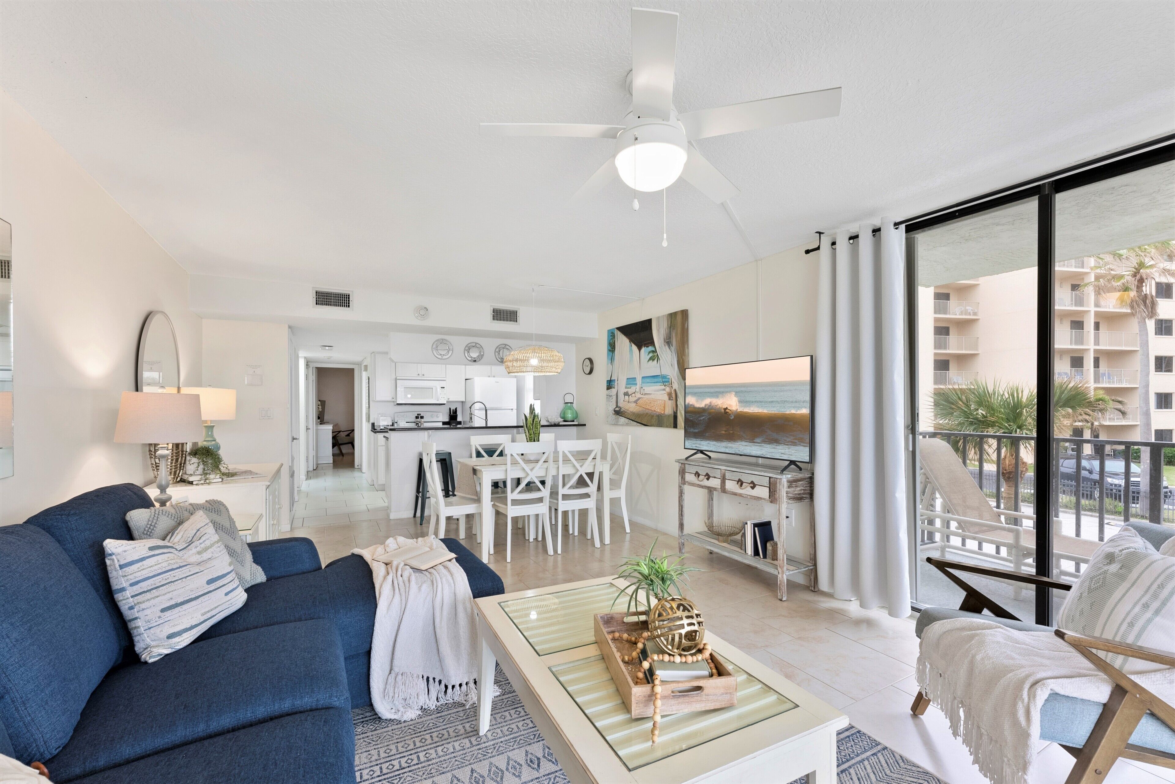 A modern living room with a blue sofa, a glass coffee table, and a dining area with white chairs.