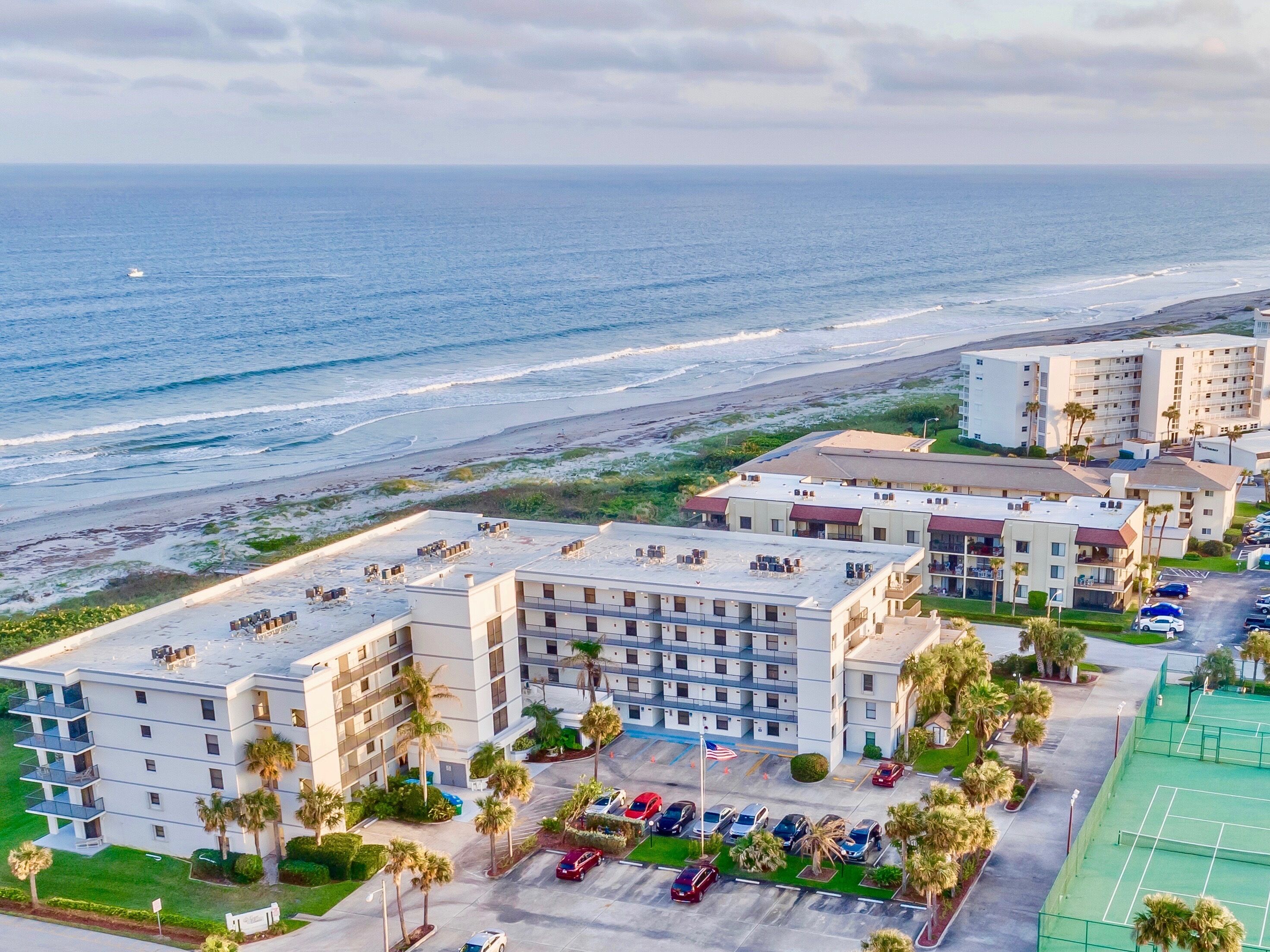 A beachfront hotel with multiple floors, a parking lot, and a tennis court.