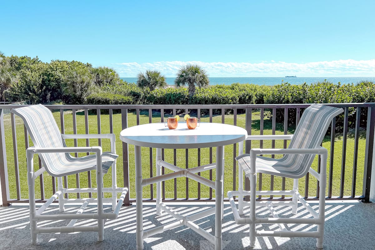 Een balkon met een ronde tafel en twee stoelen, met uitzicht op een schilderachtig zeegezicht.