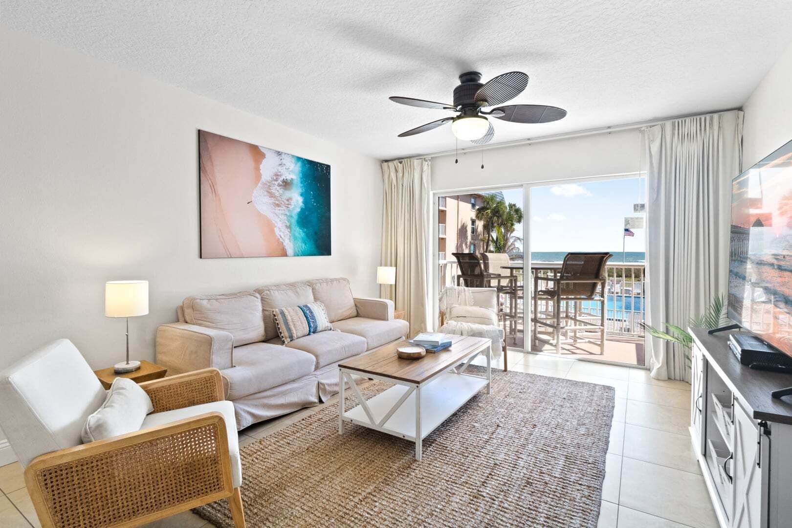 A hotel room with a balcony, a sofa, a coffee table, and a TV.