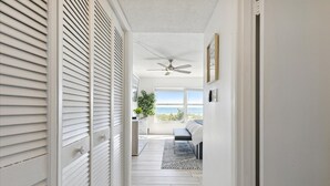 A narrow hallway with white walls, a ceiling fan, and a view of a bedroom with a bed and a window overlooking the ocean. - Spanish Main - Cocoa Beach Oceanfront Condos near Port Canaveral (Cocoa Beach)