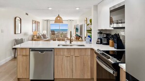 A modern kitchen with a dishwasher, stove, and dining area with a view of the sea. - Spanish Main - Cocoa Beach Oceanfront Condos near Port Canaveral (Cocoa Beach)