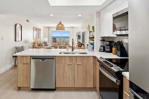 A modern kitchen with a dishwasher, stove, and dining area with a view of the sea. - Spanish Main - Cocoa Beach Oceanfront Condos near Port Canaveral (Cocoa Beach)