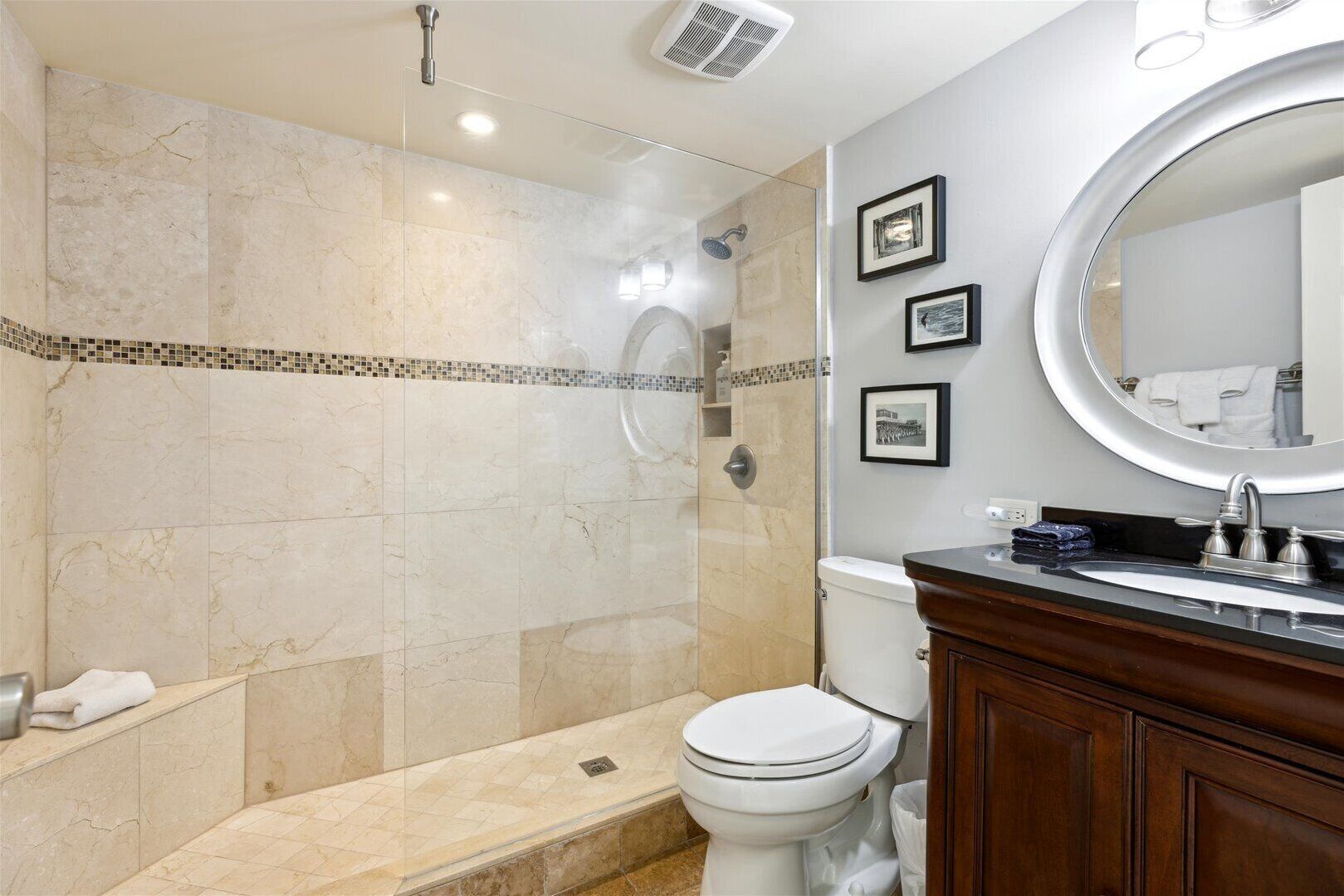 A modern bathroom with a glass-enclosed shower, a toilet, a vanity with a mirror, and framed pictures on the wall.