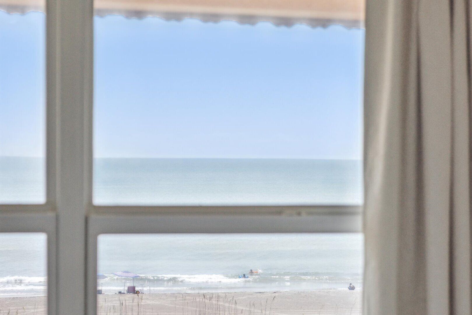 A view of a beach through a window with a clear sky.