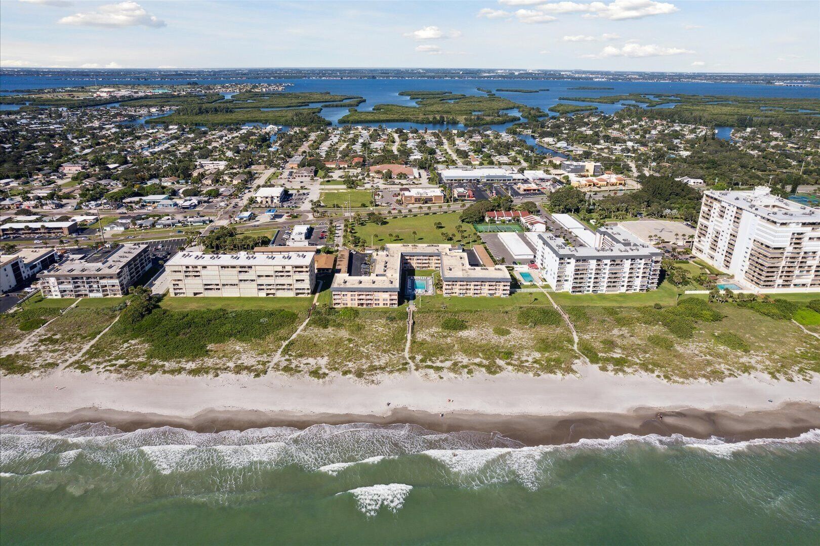 An aerial view of a coastal town with beachfront properties, a marina, and a large hotel with multiple buildings.