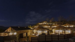 A series of wooden cabins with large windows, set against a mountainous backdrop at night. - Longlife Resort Yufuin Bettei (Yufu)
