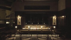 A dimly lit bar area with a long counter, framed pictures on the walls, and a view through the window. - Longlife Resort Yufuin Bettei (Yufu)