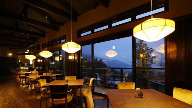 A restaurant with wooden tables and chairs, large windows with a view of a mountain, and hanging lamps. - Longlife Resort Yufuin Bettei (Yufu)