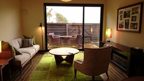 A living room with a sofa, a round coffee table, and wicker chairs. There is a sliding glass door leading to an outdoor area with a wooden deck and a fence. - Longlife Resort Yufuin Bettei (Yufu)