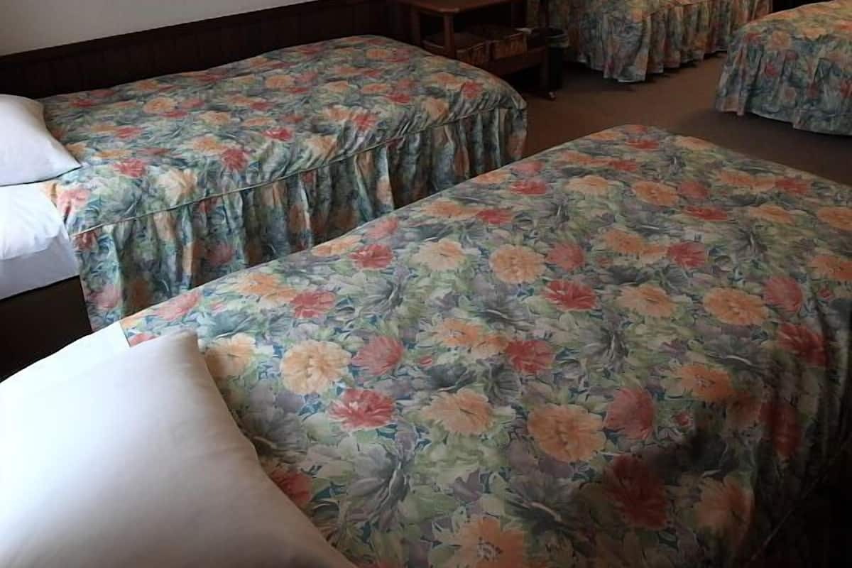 Habitación de hotel con tres camas individuales, cada una con ropa de cama floral. Hay una mesita pequeña y un perchero.