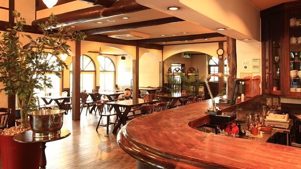 A restaurant with a curved wooden bar, wooden ceiling beams, and large windows allowing natural light. - Hakuba Pension Karunaju (Hakuba)