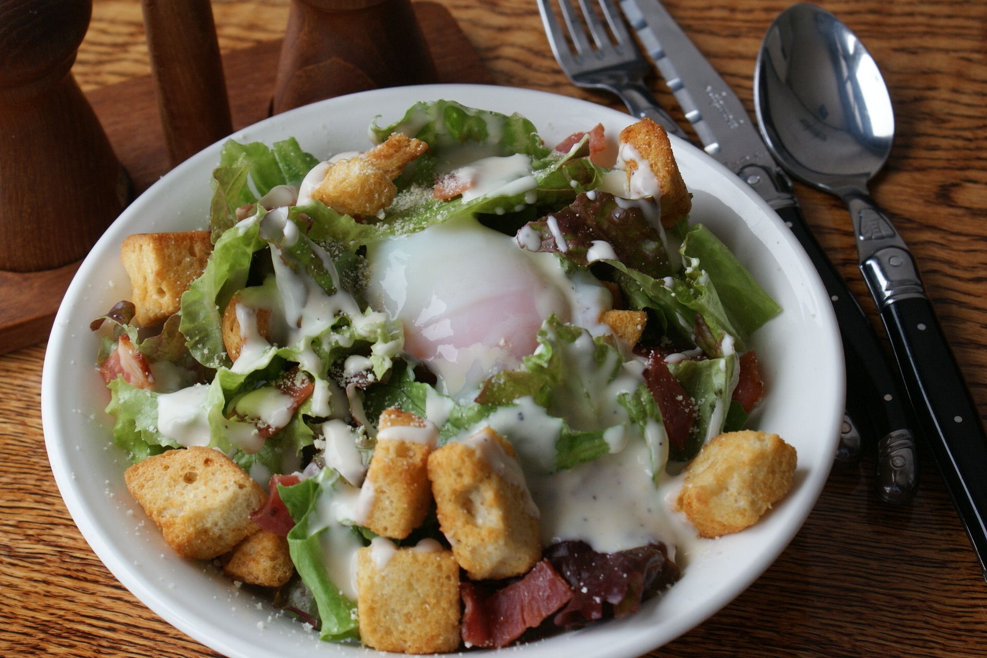 A salad with croutons and a poached egg on a white plate.