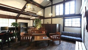 A spacious room with wooden beams, a large window, a sofa, a coffee table, and a desk with a computer. - Hakuba Pension Karunaju (Hakuba)
