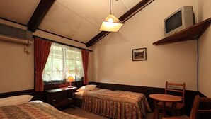 A hotel room with two beds, a desk with a lamp, a TV on a shelf, and a chair. - Hakuba Pension Karunaju (Hakuba)