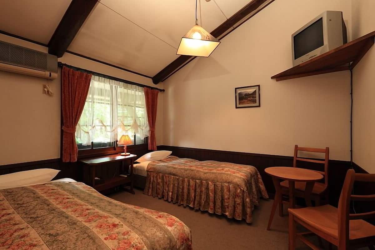 Habitación de hotel con dos camas, un escritorio con lámpara, un televisor en una estantería y una silla.