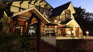 A building with a brick facade, a sign reading "Pension Karunaju," and outdoor seating with tables and umbrellas. - Hakuba Pension Karunaju (Hakuba)