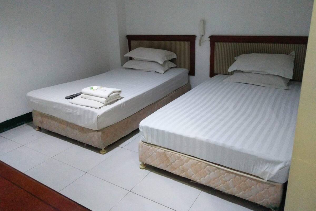 Dos camas individuales con sábanas blancas, cabeceros de madera y suelo de baldosas.