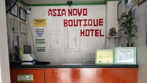 Vastaanottoalue, jossa on puinen tiski, kyltti, jossa lukee ”Asia Novo Boutique Hotel”, ja kyltti, jossa lukee ”Kassa”.
