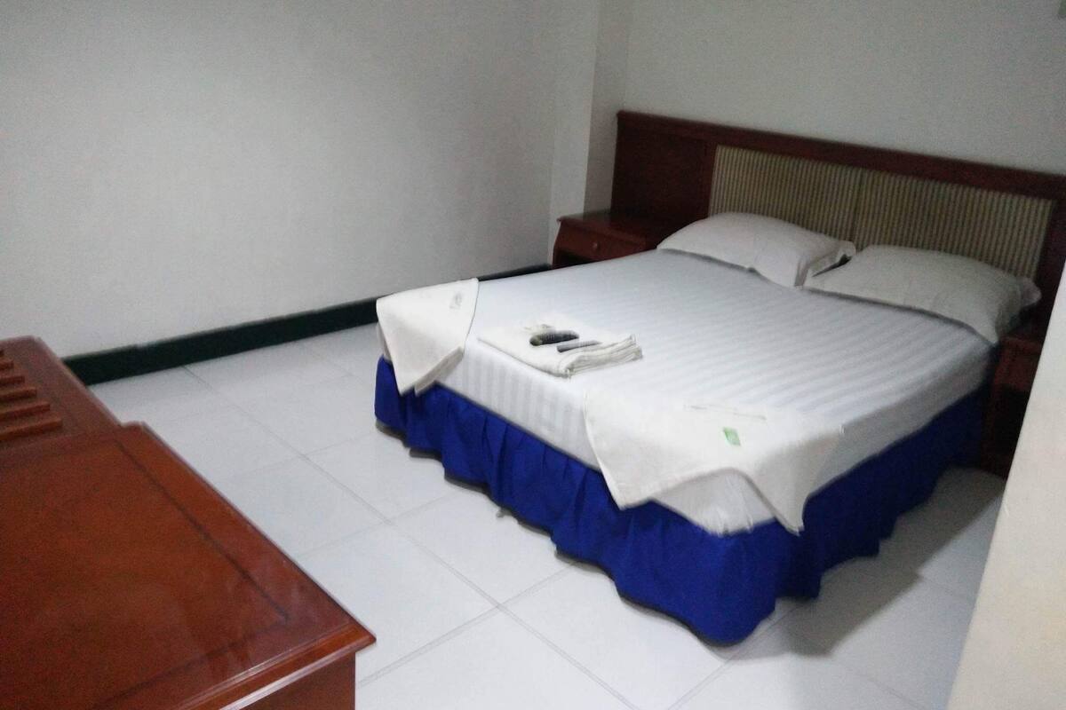 Una habitación de hotel con una cama, una mesita de noche de madera y una colcha azul.