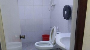 Pieni, yksinkertainen kylpyhuone, jossa on wc, bidee ja punainen ämpäri.