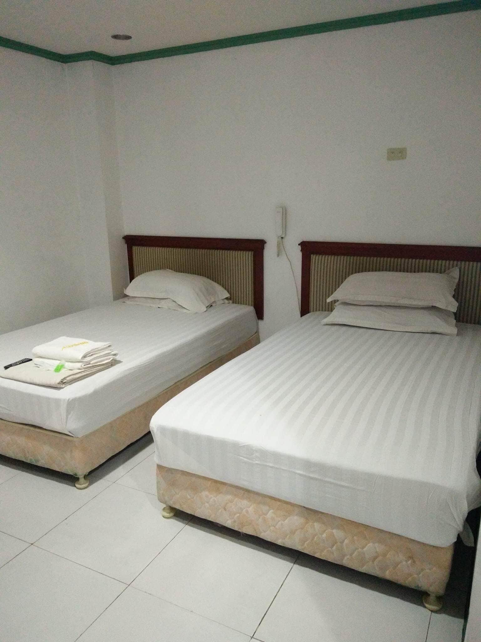 Two single beds with wooden headboards, white bedding, and a tiled floor in a hotel room.
