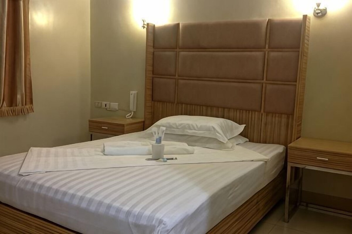 A neatly made bed with a headboard, a bedside table with a lamp, and a wall-mounted phone.