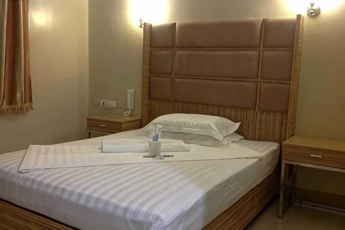 A neatly made bed with a headboard, a bedside table with a lamp, and a wall-mounted phone.