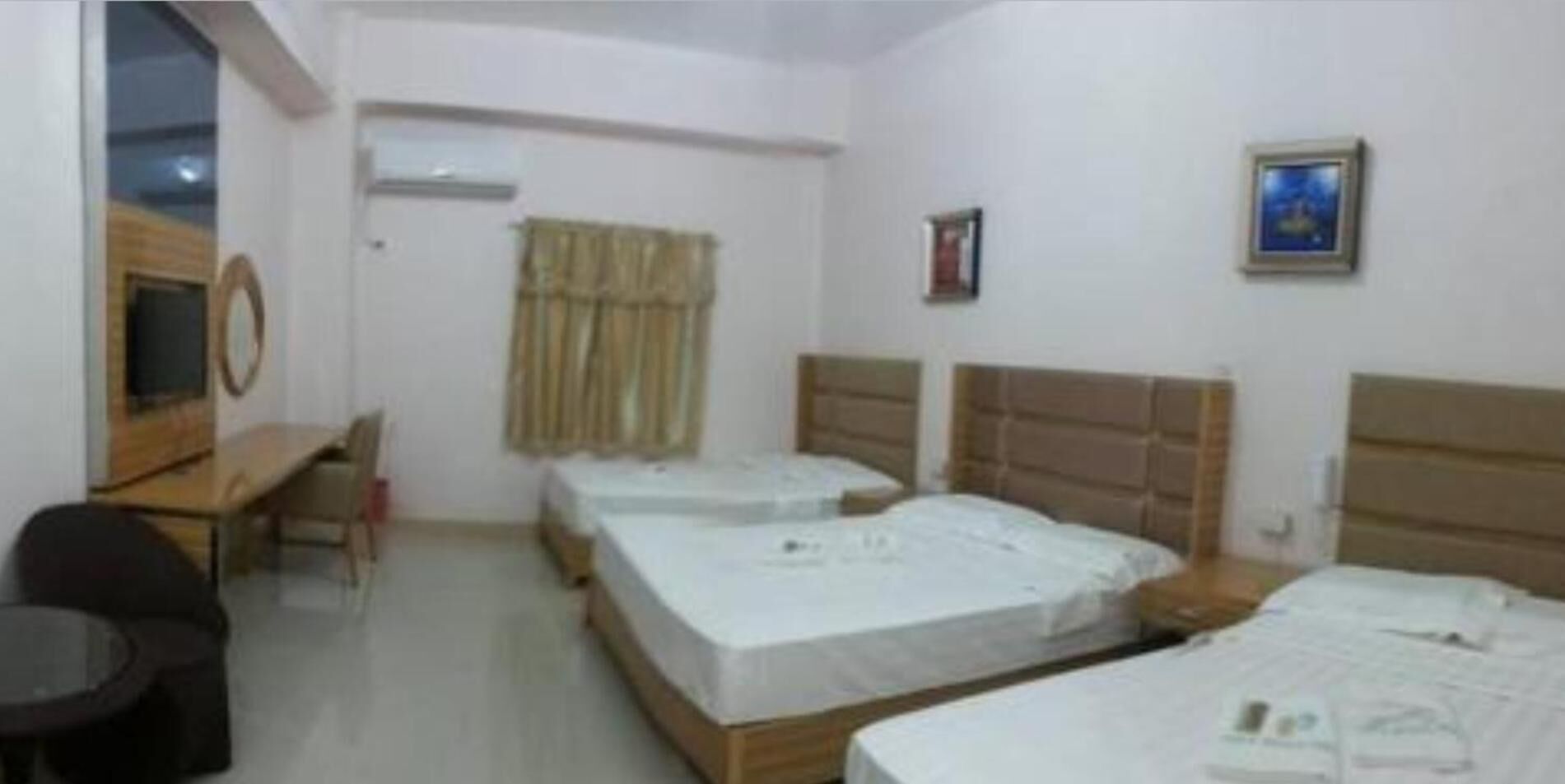 Habitación de hotel con tres camas individuales, un escritorio, una silla, un televisor y una ventana con cortinas.