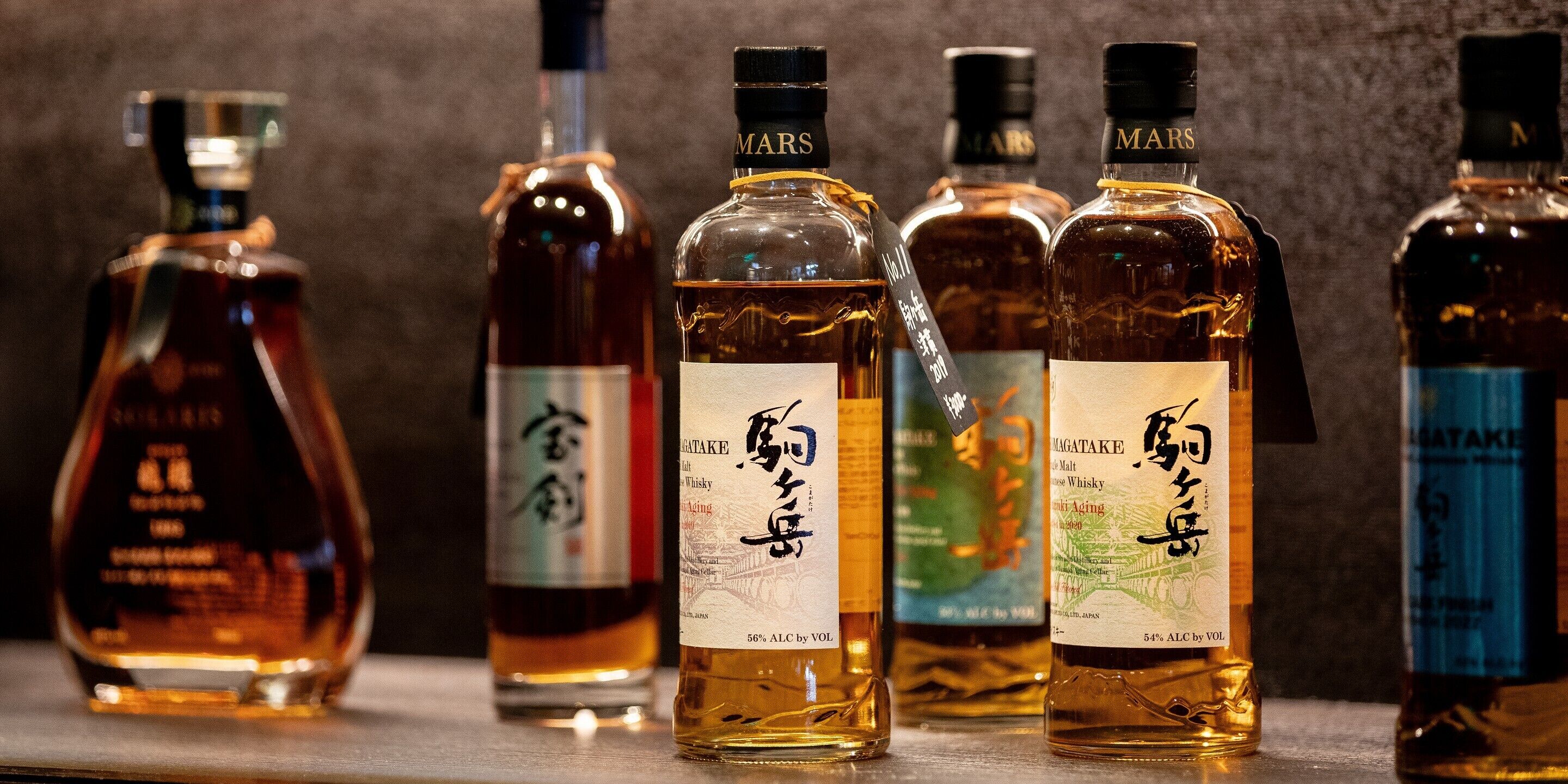 A row of whisky bottles with labels, some featuring text and others with images.