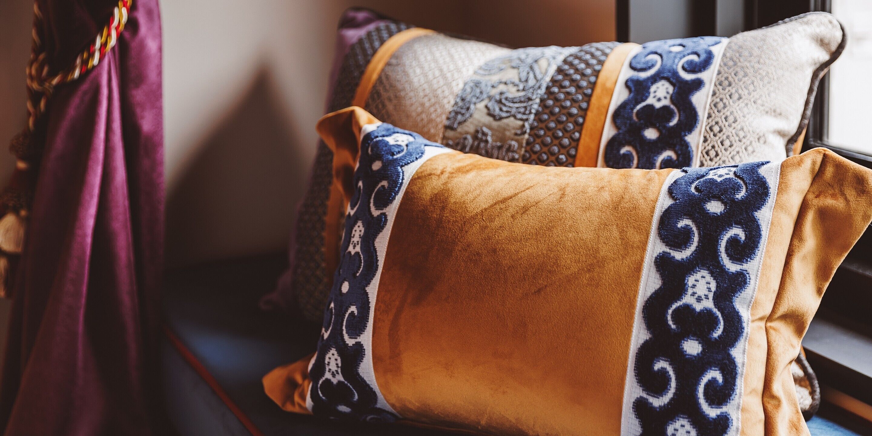 A close-up of two decorative pillows with intricate patterns, placed on a window sill.