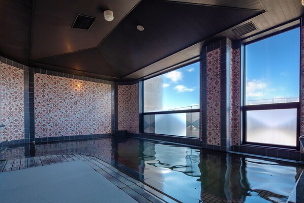 A large indoor swimming pool with patterned walls and a clear view of the sky through large windows.
