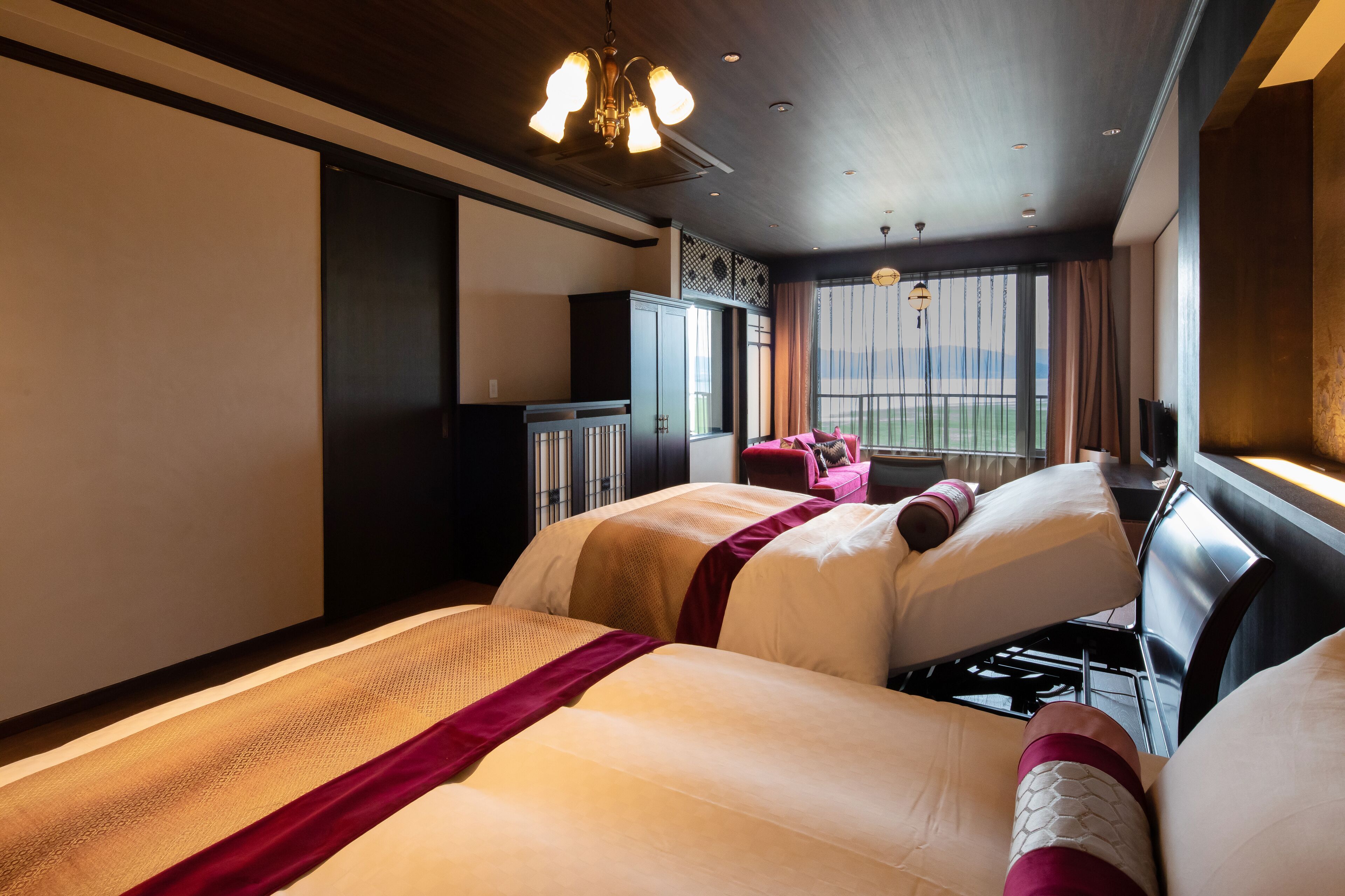 Une chambre d’hôtel avec deux lits, une grande fenêtre avec des rideaux, un luminaire au plafond et une vue sur l’extérieur.