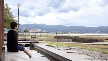 A person sitting on a wooden platform overlooking a body of water with mountains in the background.