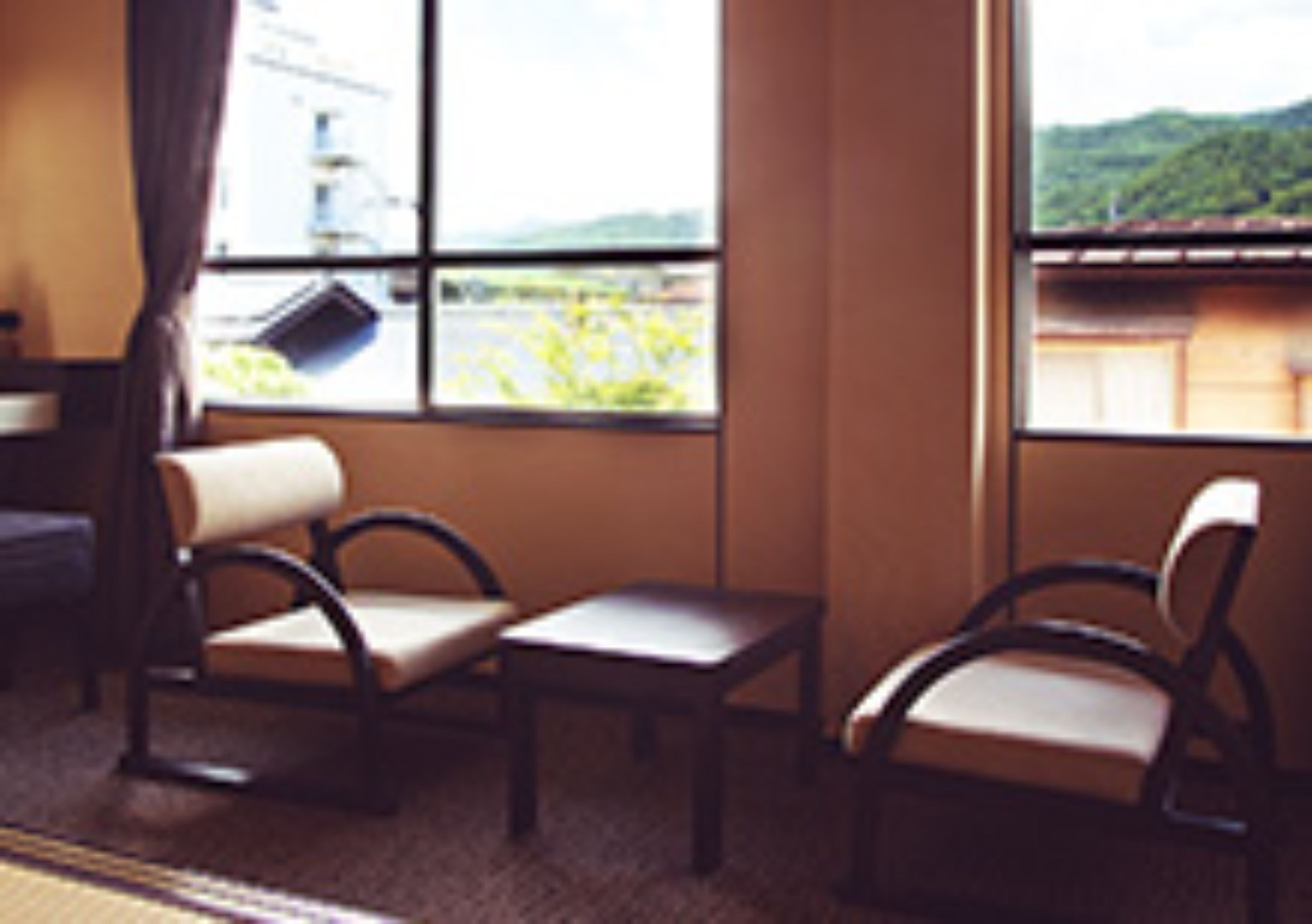 A room with two chairs and a small table, large windows with a view of greenery and a building.