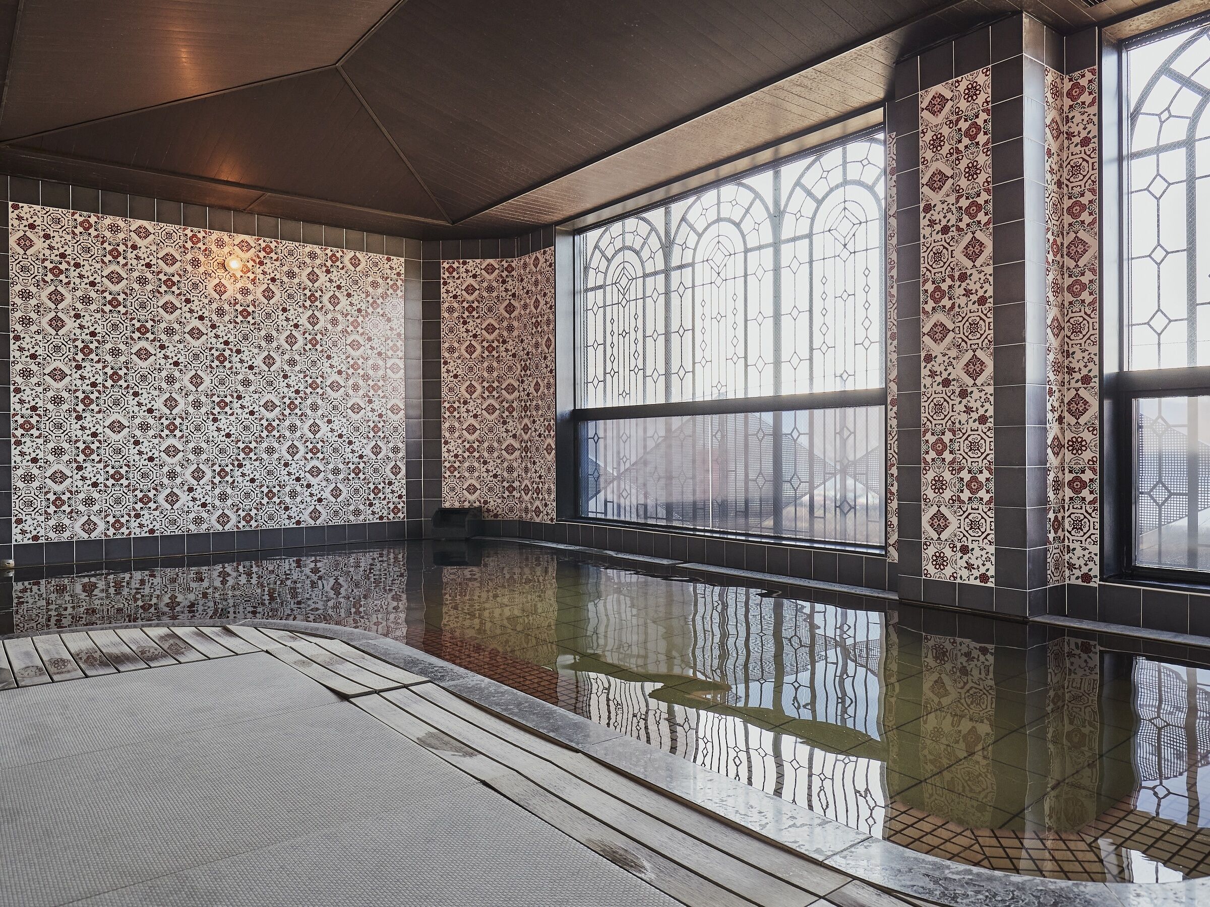 Een modern binnenzwembad met getextureerde tegels en grote ramen die de omgeving weerspiegelen.