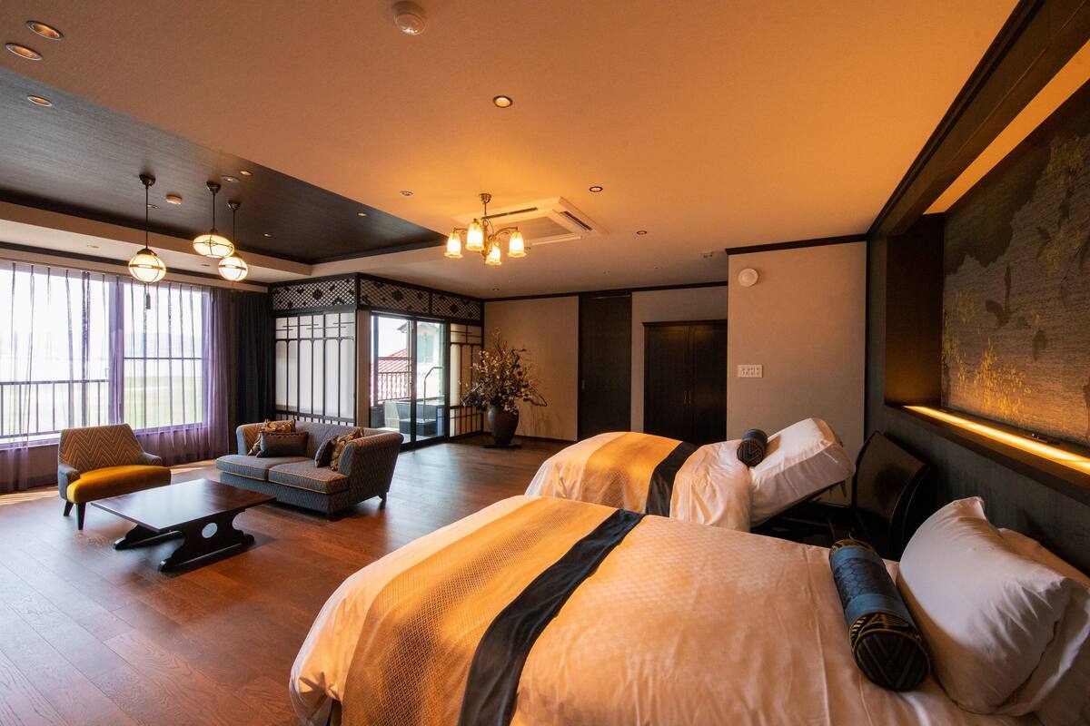 Une chambre d’hôtel avec deux lits, un canapé, une table à manger et une grande fenêtre avec des rideaux.