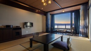 Habitación de hotel con una mesa grande, sillas, televisor y vista al mar.