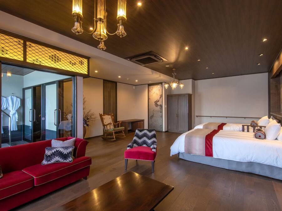 Una habitación de hotel moderna con una cama grande, un sofá rojo, una mesa de centro de madera y una zona de estar con una silla y una mesa pequeña.