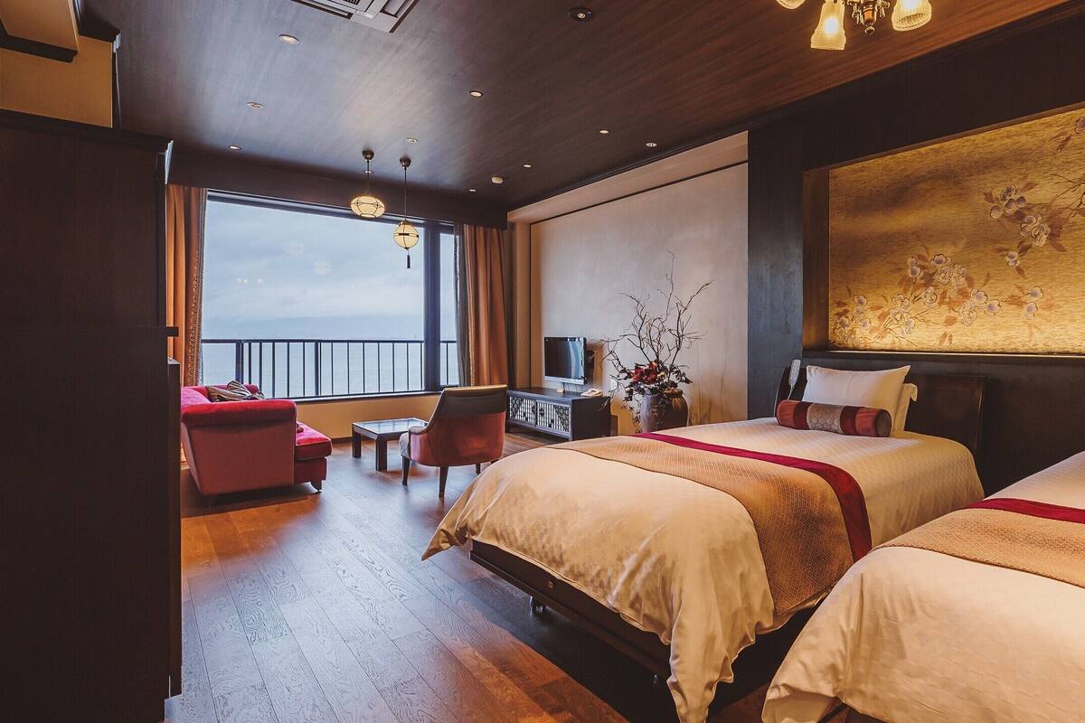 Une chambre d’hôtel avec deux lits, un bureau, une chaise et une grande fenêtre donnant sur un beau paysage.