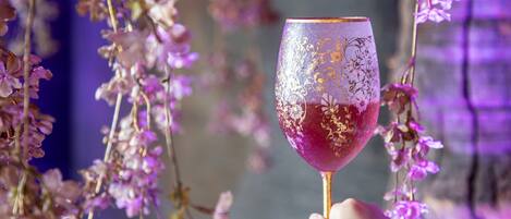 A hand holding a wine glass with a gold pattern, surrounded by purple flowers.