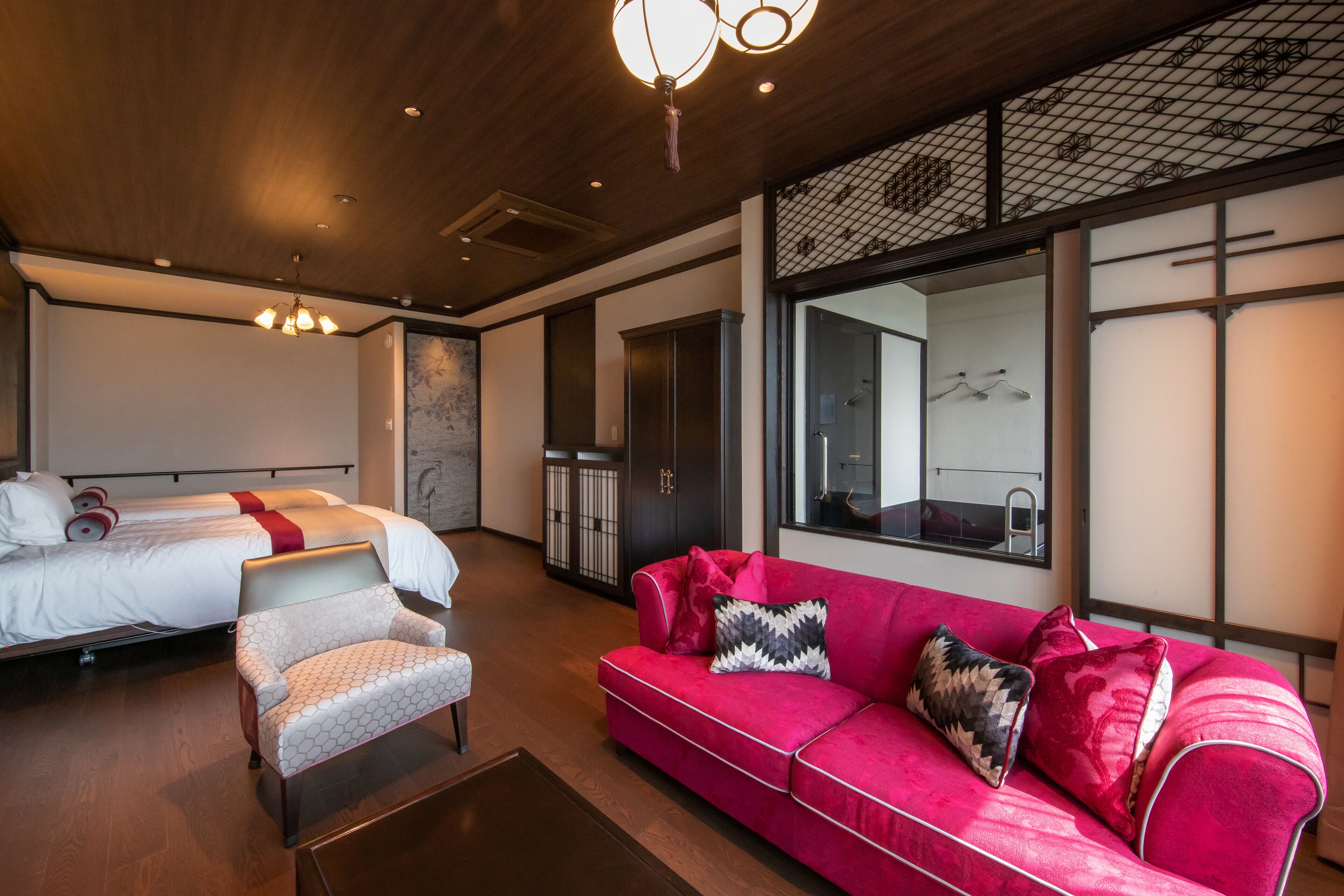 Een moderne hotelkamer met een bed, een rode bank, een fauteuil en een grote spiegel.