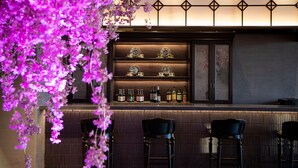 Zona de bar con estantes que exhiben botellas y teteras, taburetes de bar y un panel decorativo en la pared.