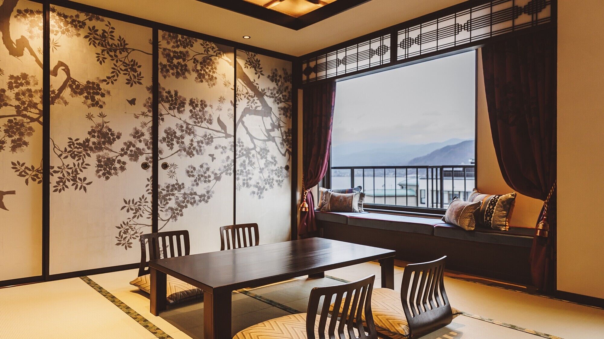 Ein traditioneller Raum mit Tatami-Böden, einem niedrigen Tisch und Stühlen, einem Shoji-Bildschirm mit floralen Mustern und Meerblick durch ein großes Fenster.