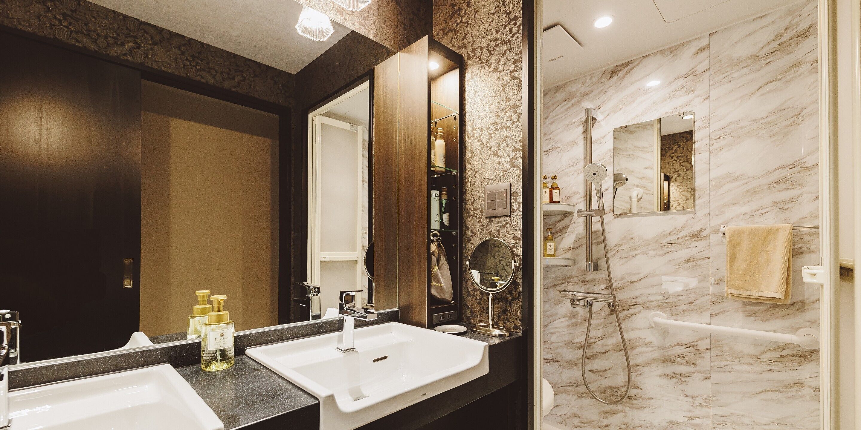 A modern bathroom with a large mirror, two sinks, a shower with a glass door, and marble walls.