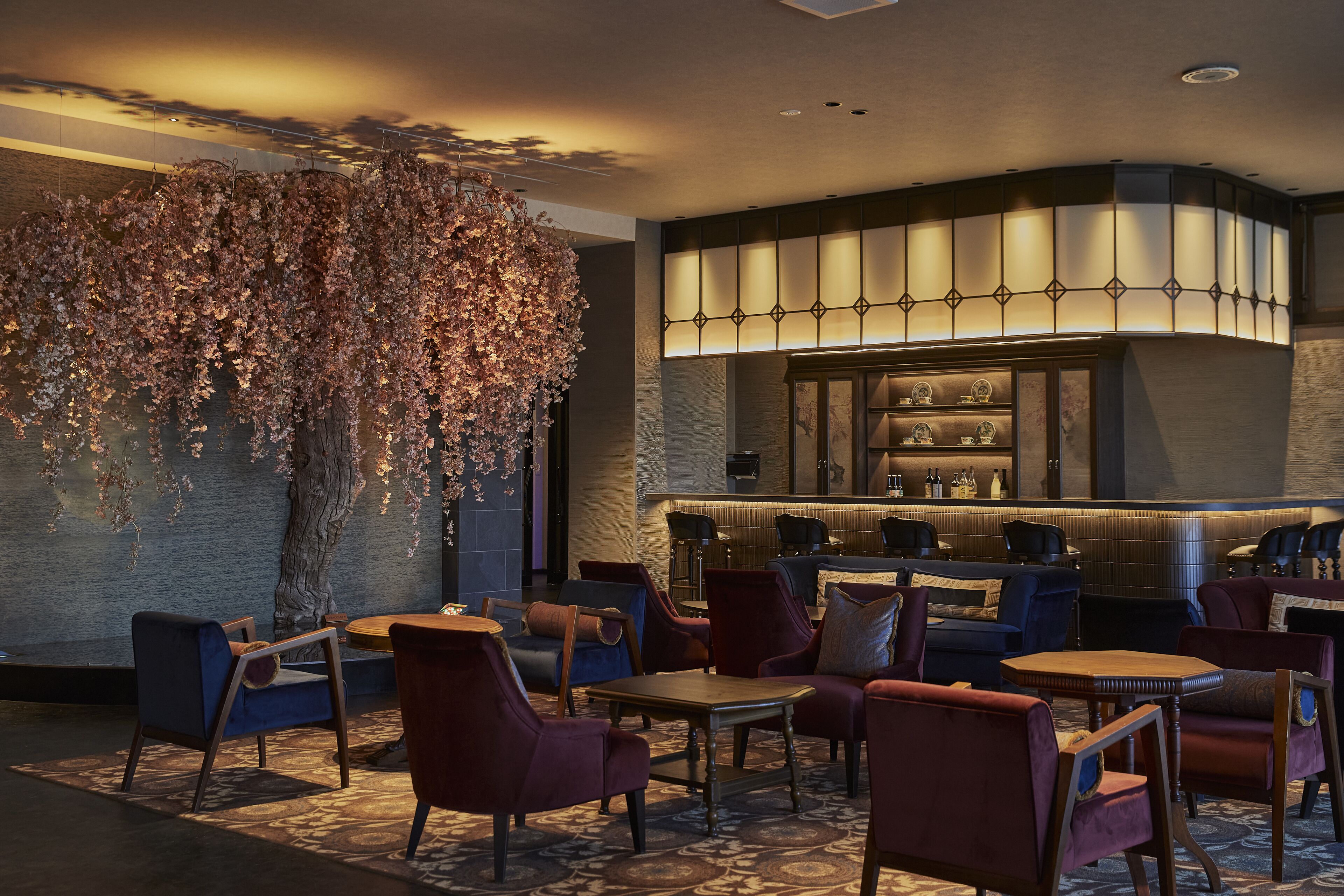 A modern lounge area with a large tree, comfortable seating, and a bar with shelves of bottles.
